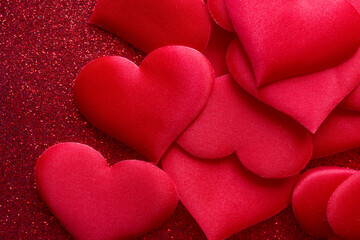 Heap of soft fabric hearts on a sparkling red texture. Festive backdrop for love messages, sympathy cards, or invitations. Bright passion symbol wallpaper. Photo
