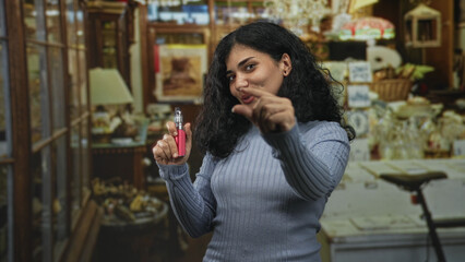 Woman holding vape device and pinching fingers to show small size inside a building; playful curiosity.