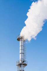 Top of smokestack with white steam or smoke against blue sky.