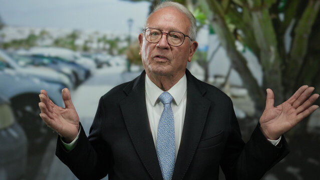 Senior man in a suit gesturing outdoors on a street background, reflecting a business environment. - Powered by Adobe