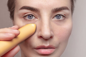 Close up crop photo of Caucasian woman with blue eyes using microcurrent facial toning device at home. Beauty popular device with LED looks after eyes