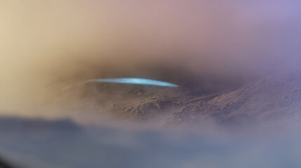 Glowing blue lake in misty mountain crater at dawn, atmospheric light and soft pastel haze creates mysterious mood