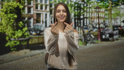 Fototapeta premium Young woman makes finger heart gesture with hands while smiling on street near building and bikes; youthful joy.