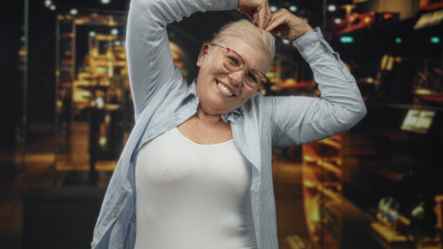 Woman raises hands above head and smiles, chest visible in a building gallery museum exhibit; joy confidence warmth.