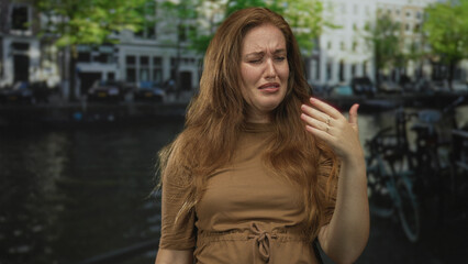 Fototapeta premium Woman pinched nose on street canal beside waterway and leaning against building facade; disgust avoidance.