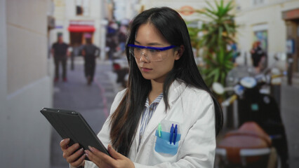Young chinese woman scientist in a lab coat and protective glasses analyzing data on a tablet outdoors on a bustling street.