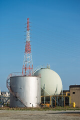 送電鉄塔と下水処理場の工業用タンク・青空に映える都市インフラとエネルギー設備景観