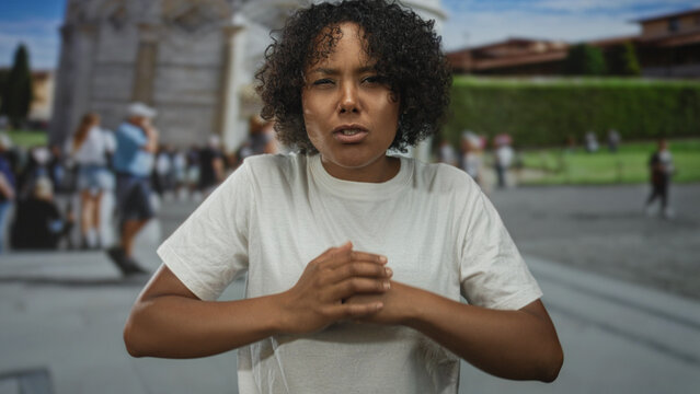 Young african american woman cracking knuckles on street near pisa tower under clear blue sky; anger release.