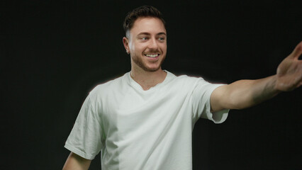 Young man with beard smiling and extending hand in friendly greeting over isolated black...