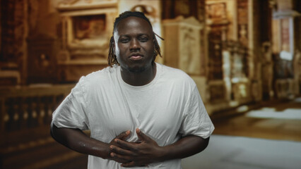 Man clutching chest inside ornate church building, hands pressed to sternum in prayerful pose; pain faith.
