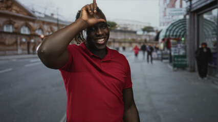 Fototapeta premium Man points finger to camera on busy city street wearing red polo shirt and smiling, dreadlocks visible and ring on finger; joy connection.