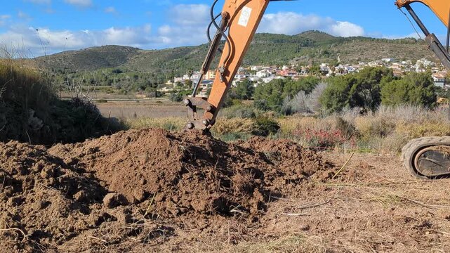 Mini excavator digging a trench and removing soil in the field