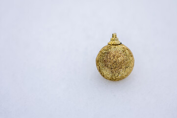 Gold glitter Christmas ball ornament on snow with clean white background and copy space, elegant and festive winter decoration suitable for holiday design, luxury branding, and seasonal advertising.