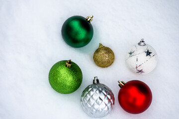 Colorful Christmas ball ornaments arranged on snow. Winter flat lay with green, red, gold, silver and white decorations, copy space, suitable for Christmas design and holiday backgrounds.