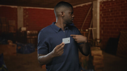 Young black man holding a creditcard, pointing finger at the card and then to his chest inside a...
