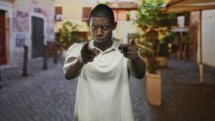 Man pointing fingers at camera on cobblestone street with planters and awning, shifting from stern to smiling expressions; playful banter.