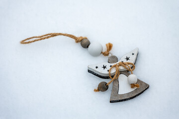Wooden angel ornament with rope and beads lying on snow. Minimal winter decoration made of natural materials, suitable for holiday design, winter backgrounds, greeting cards and seasonal decor.