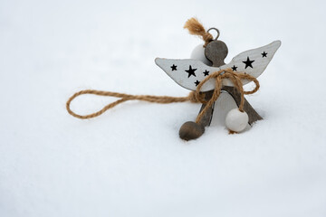 Wooden angel ornament with rope and beads placed in snow. Simple winter decoration made of natural materials, suitable for holiday backgrounds, greeting cards and seasonal design.