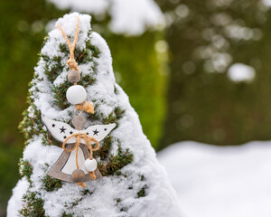 Wooden angel ornament hanging on a snow covered evergreen tree. Natural winter decoration with rope and beads, suitable for holiday backgrounds, seasonal design and greeting cards.