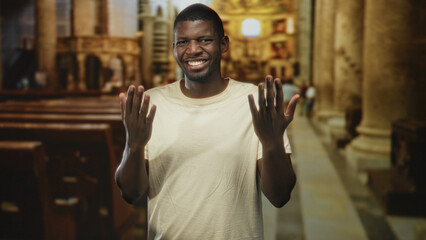 Man clapping hands in a church building among wooden pews and stone columns, shirt visible; faith...