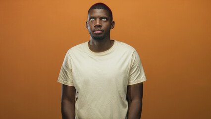 Man face looking up in orange studio wearing beige t shirt, neutral expression with subtle head tilt and relaxed arms; quiet contemplation.