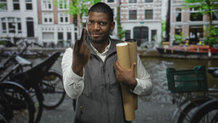 Man holding rolled blueprints and raising middle finger, hand visible, on a canal street with...
