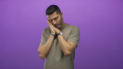 Man with hands pressed to cheek and closed eyes in purple studio wearing beige tshirt and wristwatch; tiredness rest reflection.