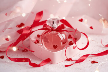 Perfumes and cosmetics. An elegant bottle of women's perfume in a soft pink gift box, decorated with a red ribbon and hearts. A gift for Valentine's Day.