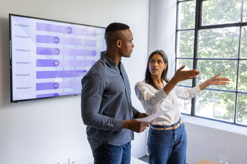 Diverse coworkers presenting data in meeting room with printed documents and bar charts by window