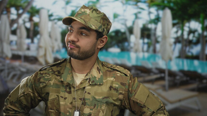 Man smirks with arms on hips by pool; confidence.