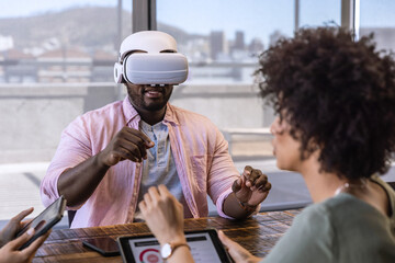 Diverse coworkers collaborating with man wearing vr headset using tablet, phone at office table
