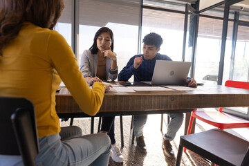 Diverse group in business attire reviewing documents at office with table and laptop