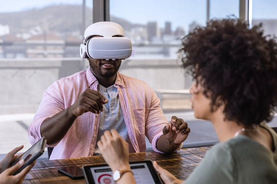 Diverse coworkers collaborating with man wearing vr headset using tablet, phone at office table - Powered by Adobe