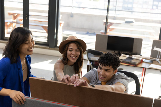 Diverse coworkers gathering around desk adjusting fabric partition panel in sunlit office - Powered by Adobe