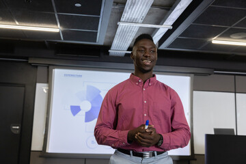 African american man with blue marker presenting pie chart on projection screen in meeting room