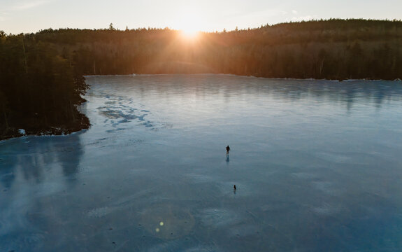Aerial view of person ice skating with dog on frozen lake in Maine