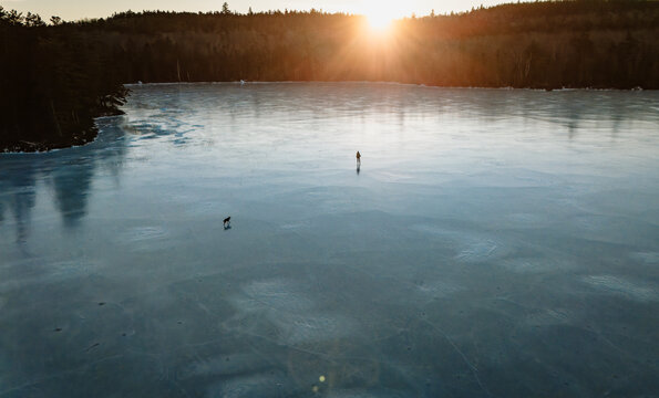Female ice skater with dog on frozen pond in Maine