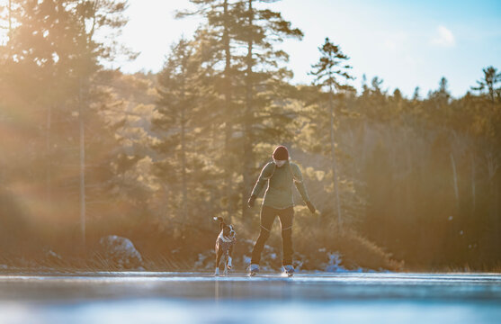 Woman ice skates with her happy dog on a frozen lake, Maine