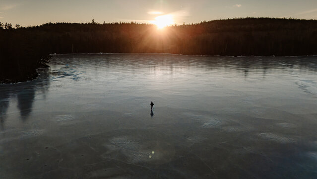 Lone ice skater at sunset on remote frozen lake in Maine.