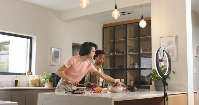 Diverse duo entering kitchen with ring light demonstrating flipping griddle and tossing salad