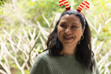 Hispanic woman standing in garden wearing textured green sweater and candy cane antler headband