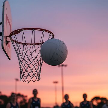 a netball hitting the net of a hoop against a beautiful pink and blue twilight sky