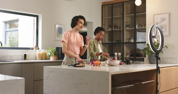 Diverse hosts gesturing at ring light chopping greens slicing pepper for salad at kitchen island