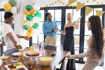 Diverse friends celebrating 21st birthday at dining table with cake, balloons, banner