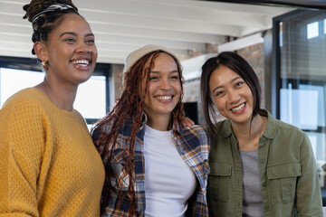 Obraz premium Diverse female coworkers posing arm-in-arm in modern office with exposed brick and glass partition