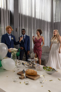 Diverse wedding party posing in modern lounge venue with bouquet by table with cupcakes