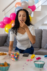 Obraz premium Teenage girl on couch eating candy from glass jar in living room decorated with balloons