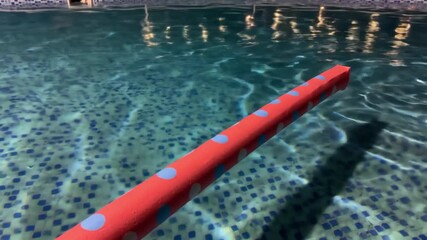 Red pool noodle floating in crystal clear water in swimming pool. Leisure and swimming concept.