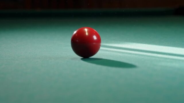 Close-up of a red billiard ball on a green table, casting a shadow under soft lighting in an indoor setting