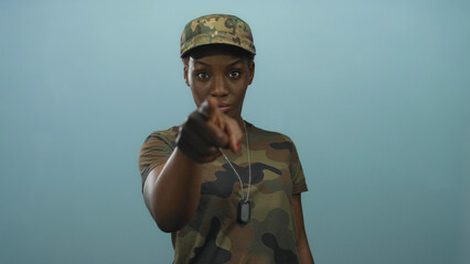 Young african american woman in camouflage uniform points finger at camera in a studio setting; authority determination confidence.